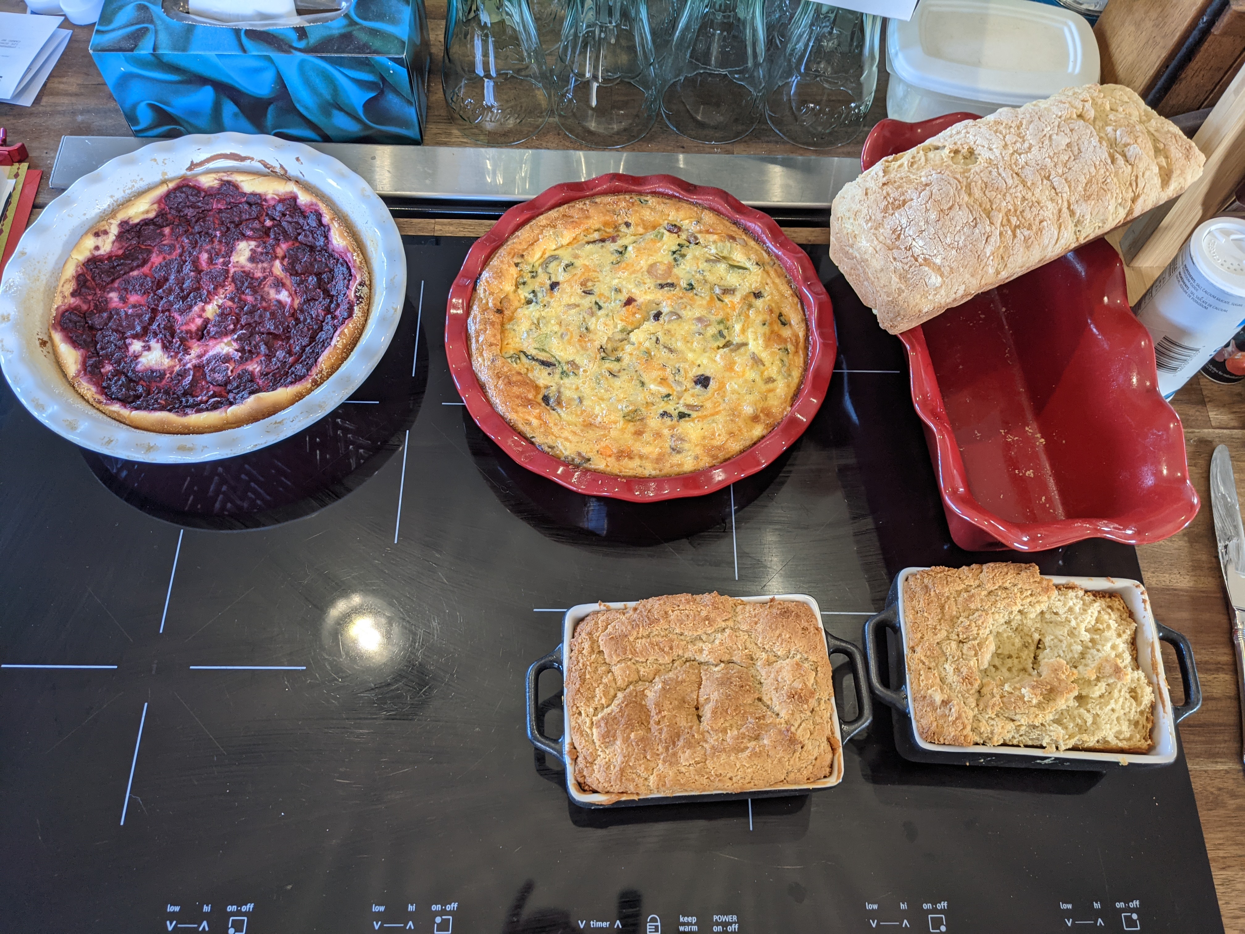 A spread of Laura's baking on the kitchen stovetop: a beet and ricotta tart, a vegetable quiche, a loaf of fresh bread, and two pans of soda bread.